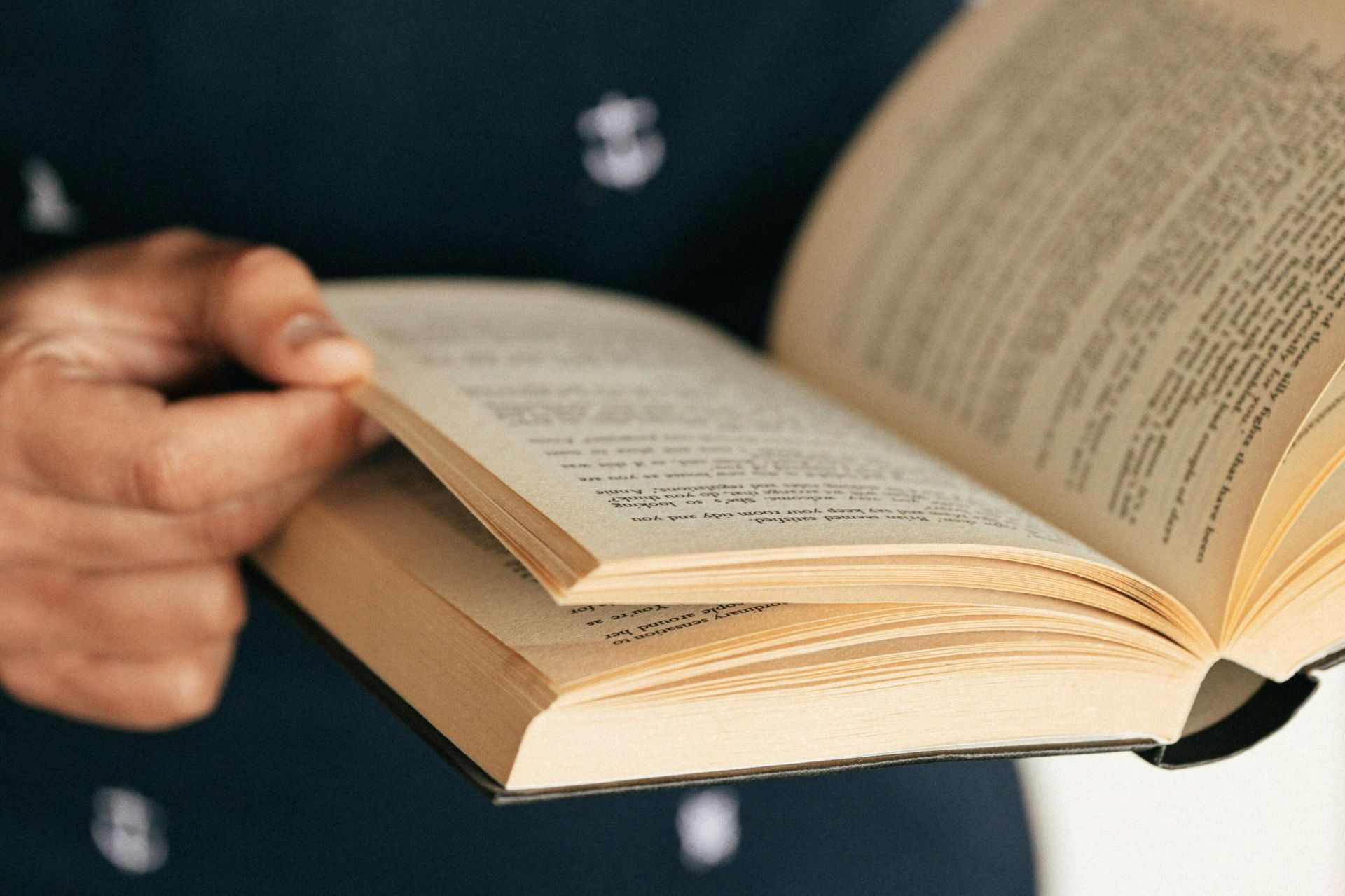 Hands holding an open book, focusing on the pages and text, creating a reading ambiance.