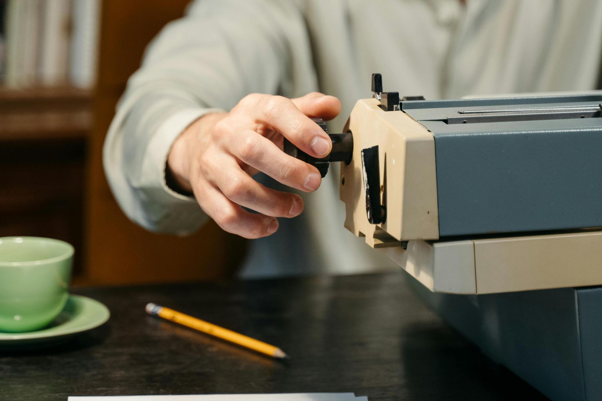 An adult man typing on a vintage typewriter at a table indoors.