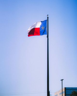 A vibrant Texas flag waving on a flagpole against a bright blue sky in Houston, Texas.